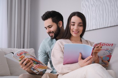Photo of Young couple reading modern magazines on sofa at home