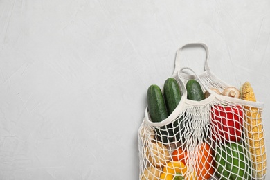 Mesh bag with fresh vegetables on light grey background, space for text