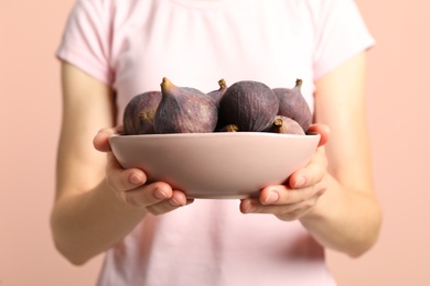 Woman holding bowl with tasty raw figs on pink  background, closeup