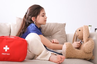 Photo of Little girl playing doctor with toy bunny on sofa indoors. Pediatrician practice