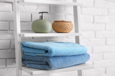 Clean soft towels and soap dispenser on shelves near white brick wall