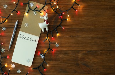 Inscription 2022 Goals written in planner and Christmas decor on wooden background, flat lay with space for text. New Year aims