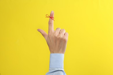 Woman showing index finger with tied red bow as reminder on yellow background, closeup