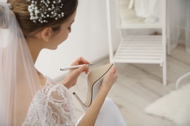 Young bride writing on her shoe indoors, closeup. Wedding superstition