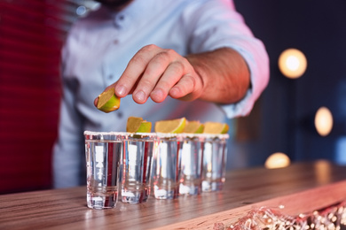 Barman putting lime on shot glass of Mexican Tequila at bar counter, closeup