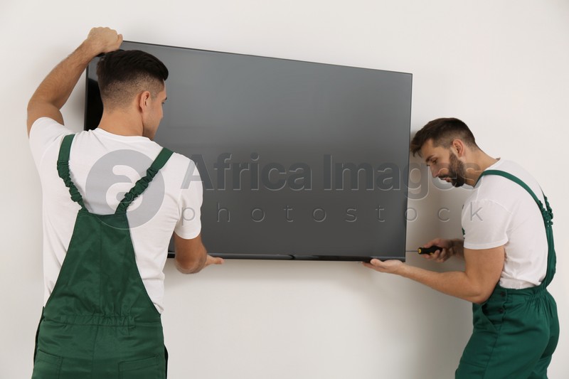 Photo of Professional technicians with screwdriver installing modern flat screen TV on wall indoors