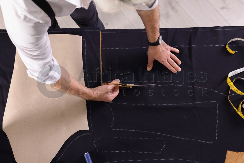 Photo of Professional tailor cutting fabric by following chalked sewing pattern at table, top view