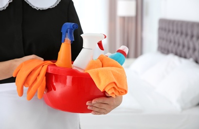 Young chambermaid with cleaning supplies in bedroom, closeup. Space for text