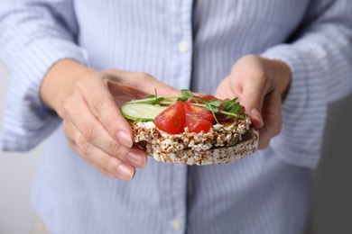 Woman holding crunchy buckwheat cakes with cream cheese, pieces of tomato and cucumber slice, closeup