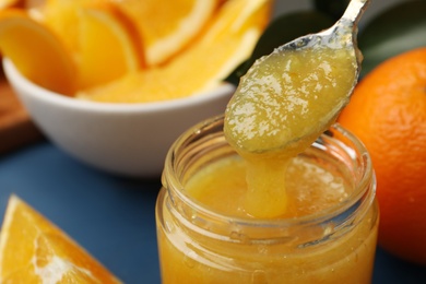 Spoon and jar with delicious orange marmalade on table, closeup. Space for text