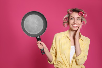 Young housewife with frying pan on pink background