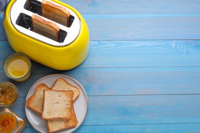 Yellow toaster with roasted bread, glass of juice and jam on light blue wooden table, flat lay. Space for text