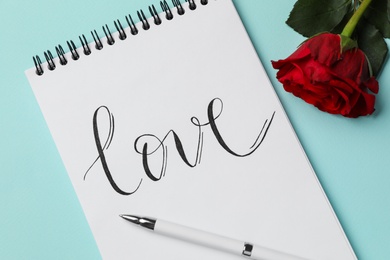 Notepad with handwritten word LOVE and rose on turquoise background, flat lay