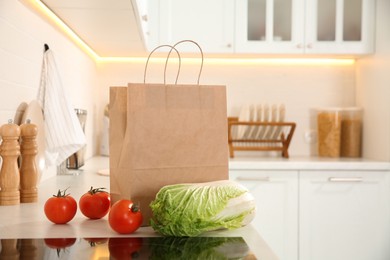 Paper shopping bag and fresh vegetables on white countertop in kitchen. Space for text