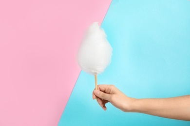 Woman holding stick with fluffy cotton candy on color background, closeup