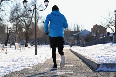 Man running along park on winter day, back view. Outdoors sports exercises