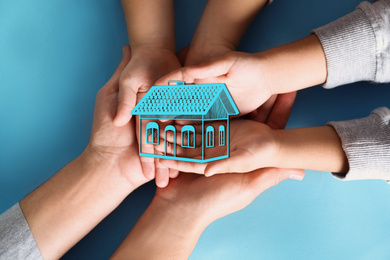 Home security concept. Family holding house on light blue background, top view