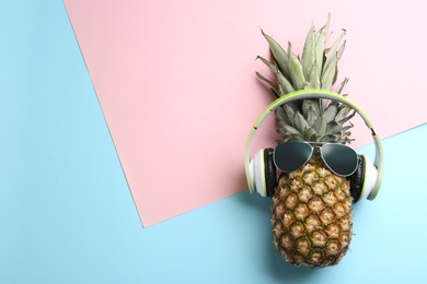 Top view of pineapple with headphones and sunglasses on color background, space for text. Creative concept