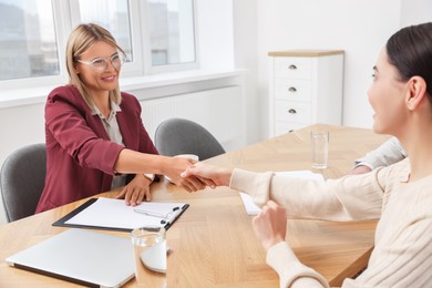 Photo of Real estate agent shaking hands with client at table in new apartment