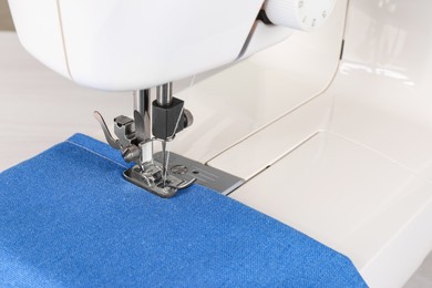 Photo of Modern sewing machine with blue cloth, closeup