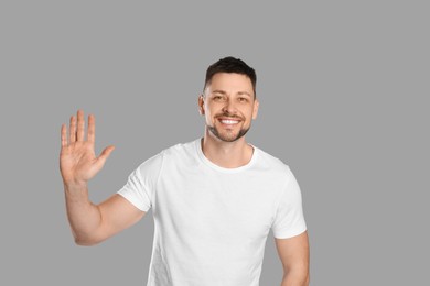 Photo of Cheerful man waving to say hello on light grey background