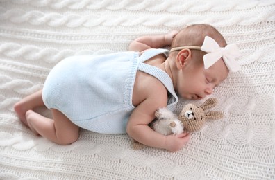 Adorable newborn baby with toy bunny sleeping on white knitted plaid, above view