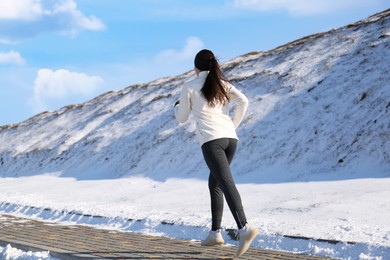 Woman running past snowy hill in winter. Outdoors sports exercises