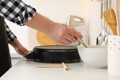 Man cooking delicious crepe on electric pancake maker in kitchen, closeup