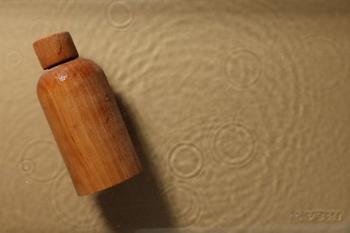 Photo of Wooden bottle of cosmetic product in water on beige background, top view. Space for text