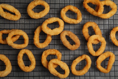 Cooling rack with fried onion rings on grey table, top view
