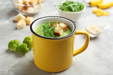 Metal mug of broccoli cream soup with croutons served on grey table