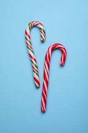 Two sweet Christmas candy canes on light blue background, flat lay
