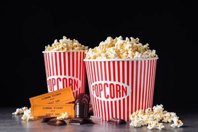 Popcorn, tickets and film footage on grey table against black background. Cinema snack