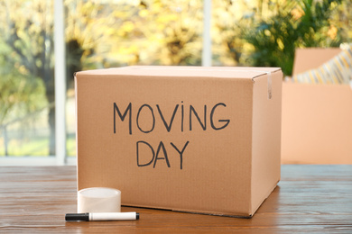 Cardboard box with words MOVING DAY and packaging items on wooden table