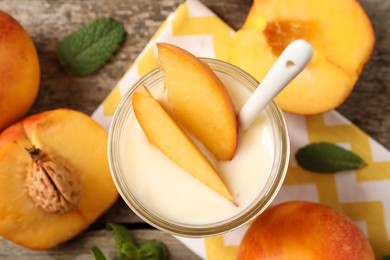 Tasty peach yogurt with pieces of fruit and spoon in glass jar on wooden table, flat lay