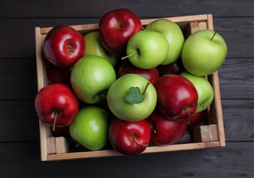 Fresh ripe red and green apples in wooden crate on black table, top view