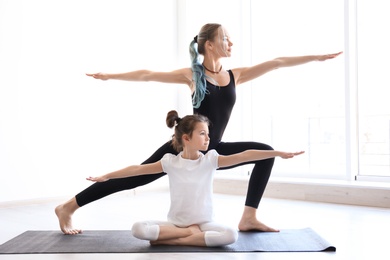 Little girl and her teacher practicing yoga in gym