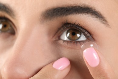 Photo of Young woman putting contact lens in her eye, closeup