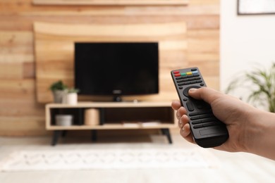 Young man switching channels on TV set with remote control at home, closeup