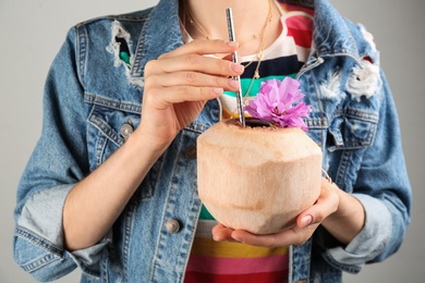 Woman holding fresh young coconut with straw on grey background, closeup