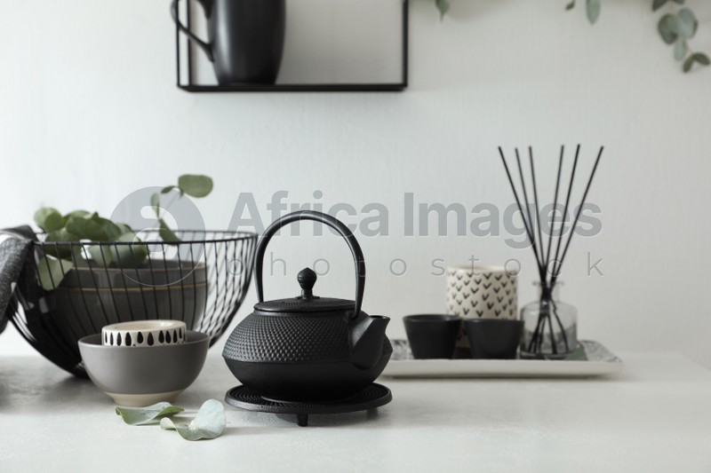 Photo of Stylish black teapot and beautiful green eucalyptus leaves on white table indoors