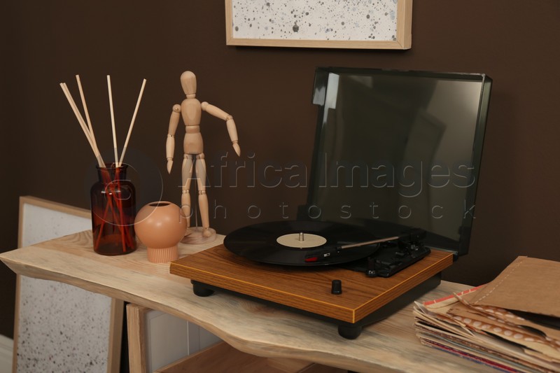 Photo of Modern turntable with vinyl disc on wooden table indoors. Interior design