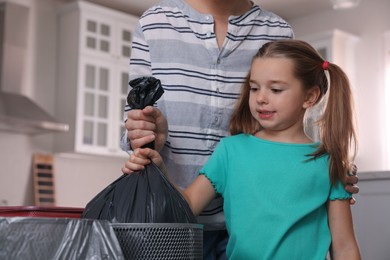 Little girl taking garbage bag out of bin in kitchen. Separate waste collection