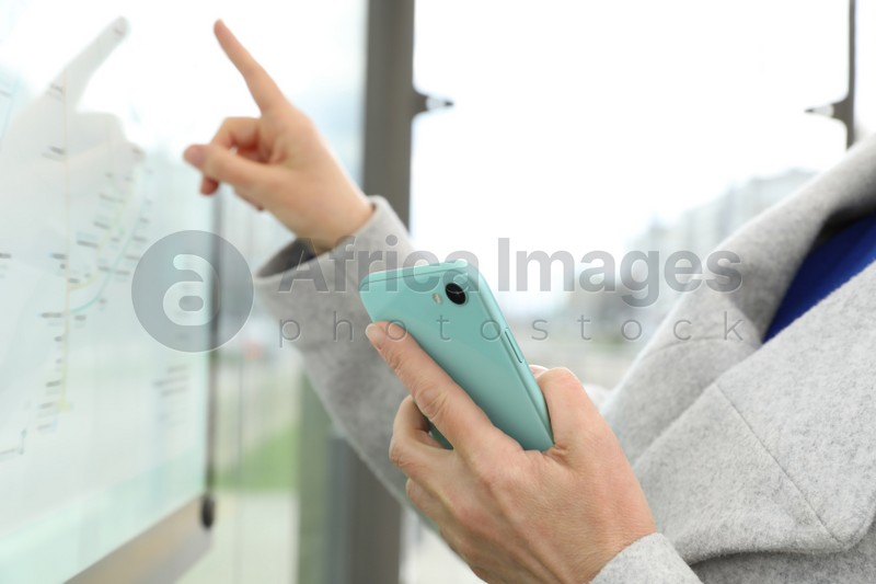 Photo of Woman with smartphone studying public transport map outdoors, closeup