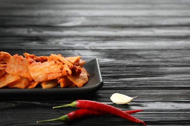 Photo of Delicious kimchi with Chinese cabbage, red chili peppers and garlic on black wooden table, space for text