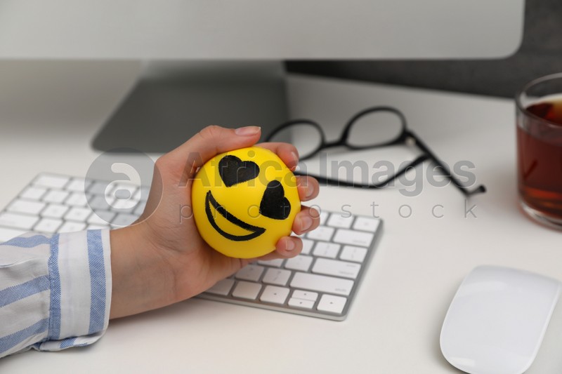 Woman squeezing antistress ball at workplace, closeup