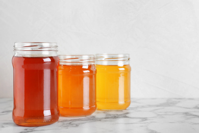 Jars with different types of organic honey on marble table against white background
