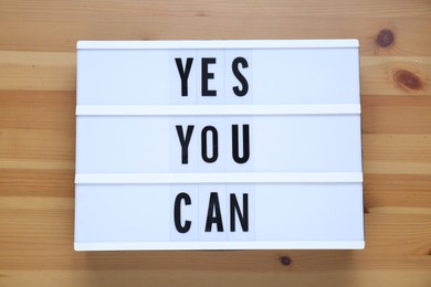 Lightbox with phrase Yes You Can on wooden table, top view. Motivational quote