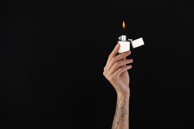 Woman holding lighter with burning flame on black background, closeup. Space for text