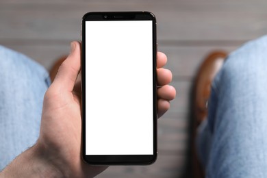 Photo of Man holding smartphone with blank screen indoors, top view. Mockup for design